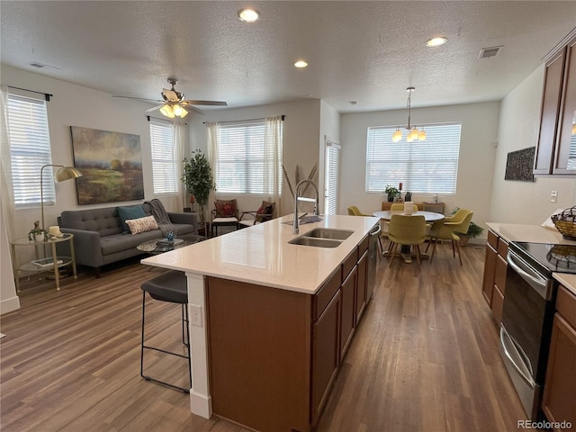 kitchen featuring dark hardwood / wood-style floors, pendant lighting, electric range, sink, and a kitchen island with sink