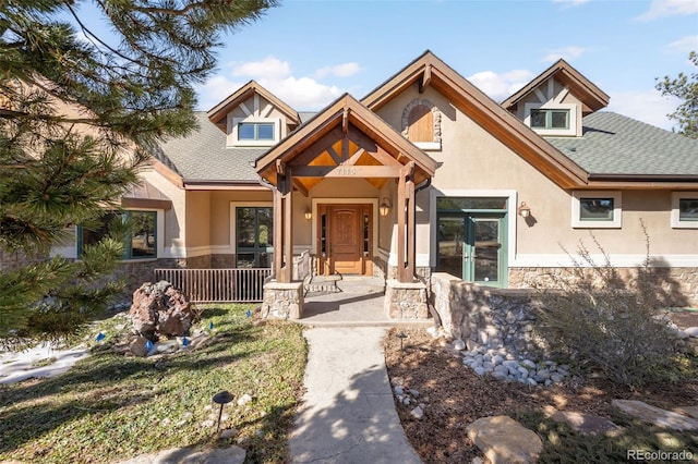 view of front of home with a shingled roof, stone siding, and stucco siding