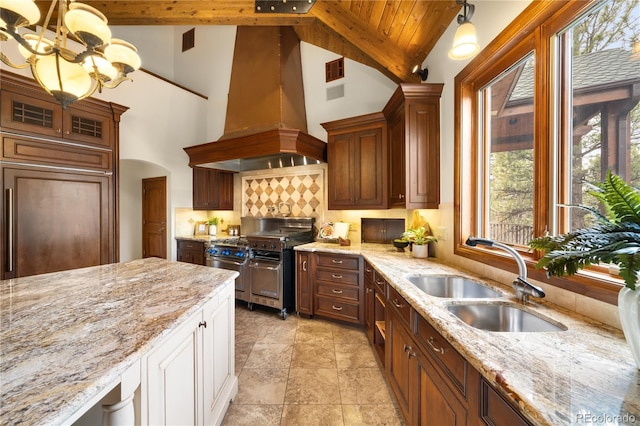 kitchen with light stone countertops, custom exhaust hood, white cabinetry, high end stainless steel range, and a sink