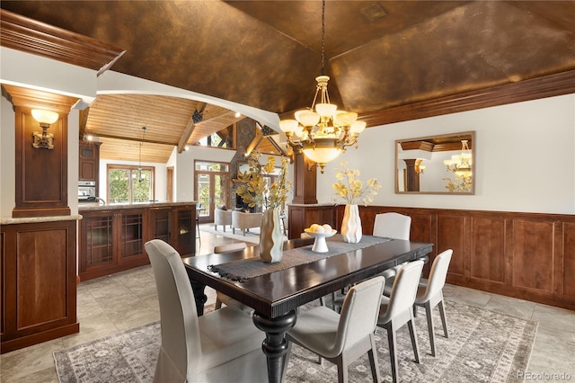 dining space featuring a wainscoted wall, lofted ceiling with beams, wooden ceiling, an inviting chandelier, and ornate columns