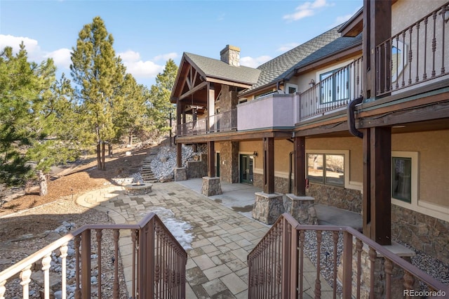 exterior space featuring a patio, a balcony, roof with shingles, stucco siding, and stone siding