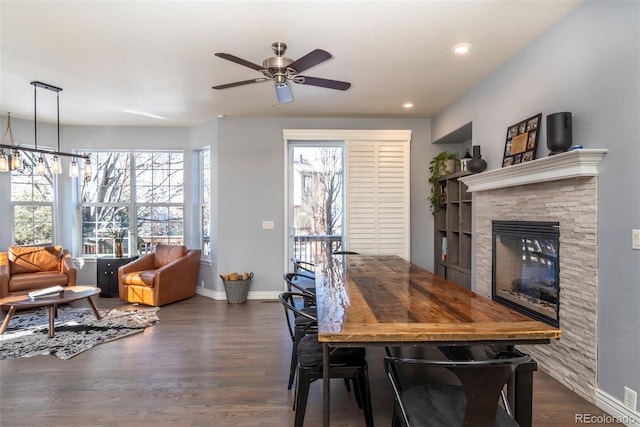 dining space featuring dark hardwood / wood-style floors, ceiling fan with notable chandelier, and a stone fireplace