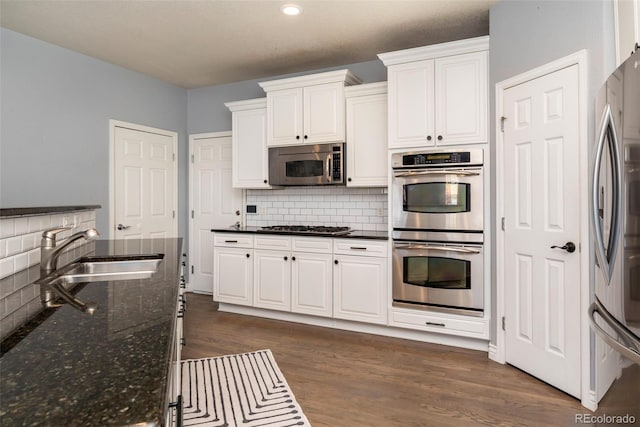 kitchen with dark hardwood / wood-style floors, sink, dark stone countertops, white cabinets, and stainless steel appliances