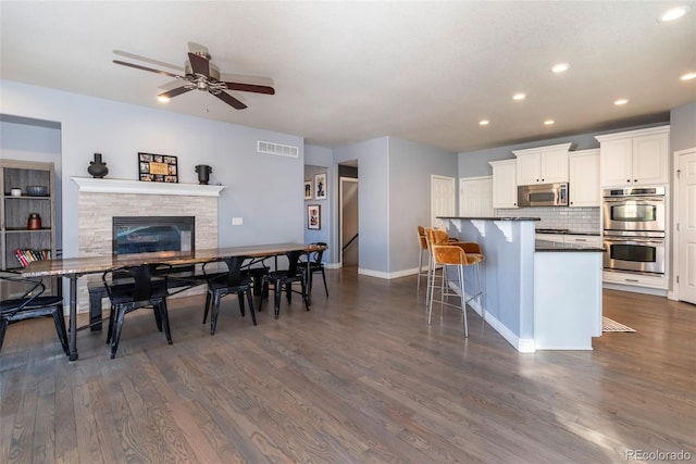 kitchen with dark wood-type flooring, a breakfast bar, stainless steel appliances, decorative backsplash, and white cabinets