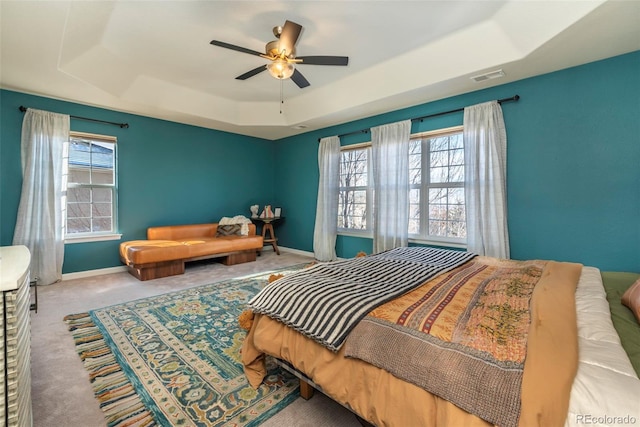 carpeted bedroom with multiple windows, a tray ceiling, and ceiling fan