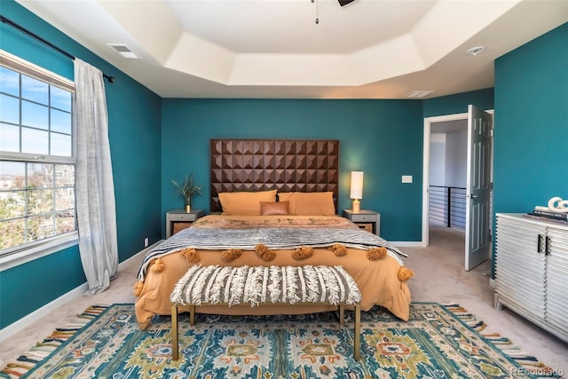 bedroom with multiple windows, light colored carpet, and a raised ceiling