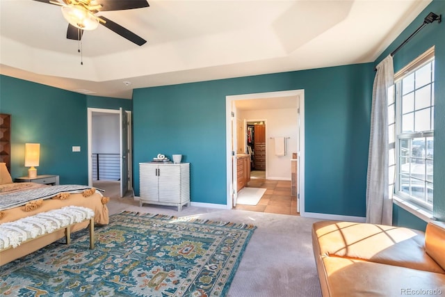 bedroom with ceiling fan, ensuite bathroom, a tray ceiling, and light carpet