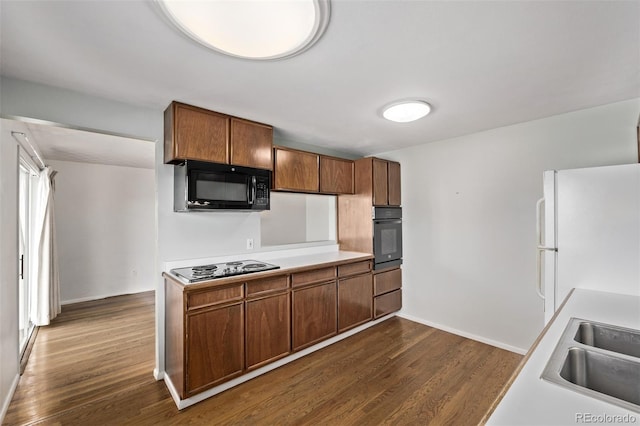 kitchen featuring dark wood-type flooring, light countertops, a sink, and black appliances