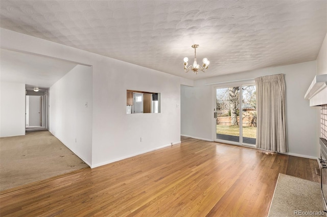 unfurnished room featuring a chandelier, a textured ceiling, light wood-style flooring, baseboards, and a brick fireplace