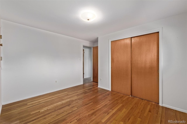 unfurnished bedroom with a closet, wood finished floors, and baseboards