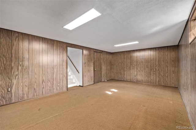 unfurnished room featuring stairway, wood walls, and light colored carpet