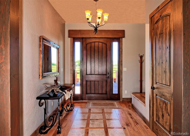 entryway with a chandelier, light wood-type flooring, and a textured wall