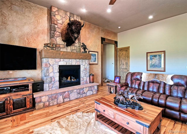living area with a textured ceiling, visible vents, a stone fireplace, recessed lighting, and hardwood / wood-style floors