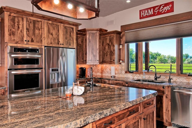 kitchen featuring a sink, a wealth of natural light, appliances with stainless steel finishes, dark stone counters, and decorative backsplash