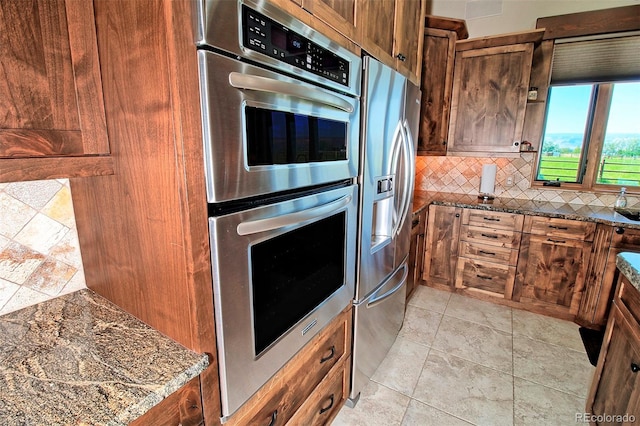 kitchen featuring dark stone countertops, brown cabinetry, decorative backsplash, and stainless steel appliances