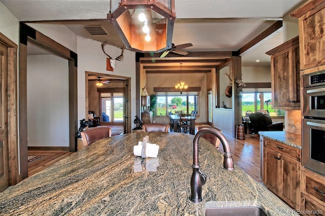 dining area featuring baseboards, visible vents, beamed ceiling, ceiling fan with notable chandelier, and wood finished floors