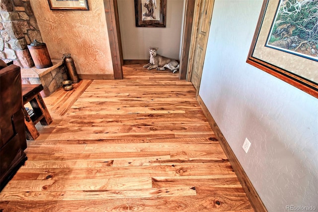 hall with light wood-style flooring, a textured wall, and baseboards