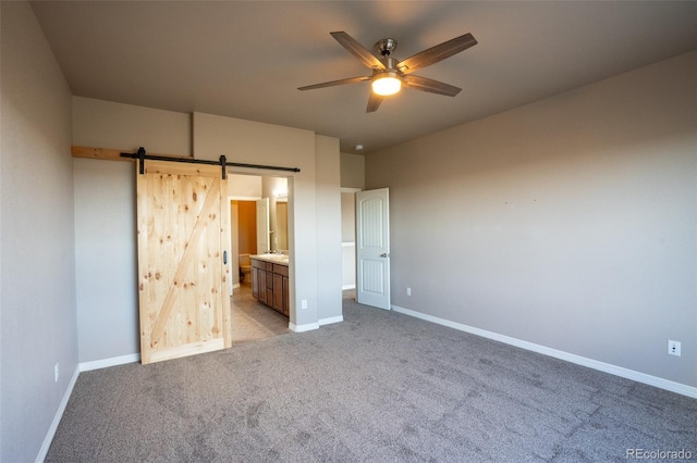 1985 Reed Grass Way, Colorado Springs, CO 80915 - unfurnished bedroom featuring a barn door, light carpet, ensuite bathroom, and a ceiling fan