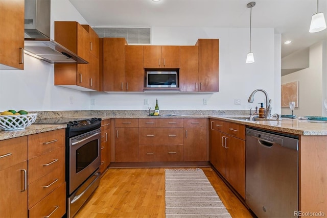 kitchen featuring light hardwood / wood-style floors, pendant lighting, sink, appliances with stainless steel finishes, and wall chimney exhaust hood