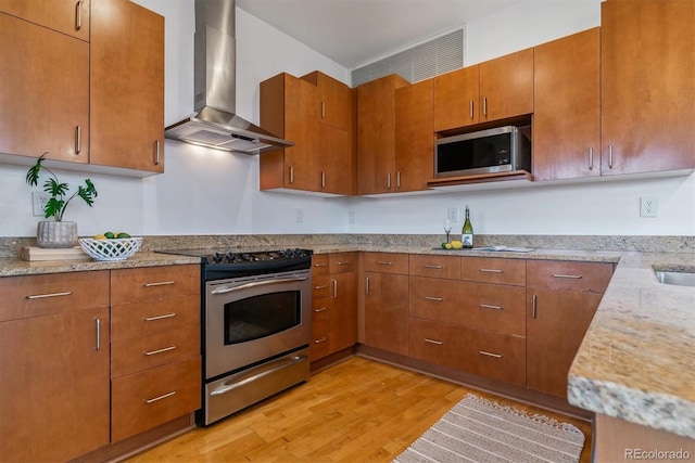 kitchen with light hardwood / wood-style floors, stainless steel appliances, wall chimney exhaust hood, light stone counters, and sink