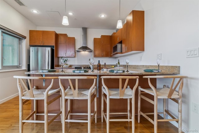 kitchen featuring decorative light fixtures, appliances with stainless steel finishes, wall chimney exhaust hood, and light wood-type flooring