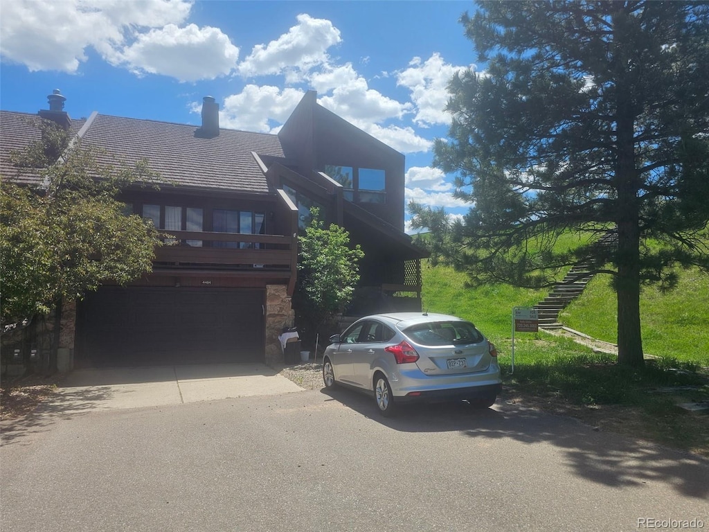 view of front facade featuring stairway, a garage, driveway, a chimney, and stone siding
