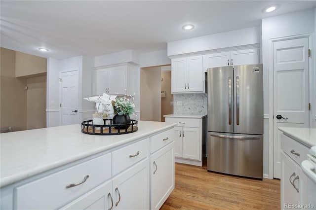 kitchen with white cabinets, backsplash, stainless steel fridge, and light wood-type flooring