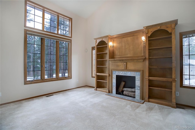 unfurnished living room with light carpet, a towering ceiling, a tile fireplace, and a healthy amount of sunlight