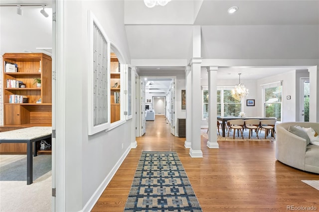 foyer with a notable chandelier, hardwood / wood-style floors, track lighting, and ornate columns