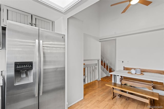 kitchen with stainless steel refrigerator with ice dispenser, ceiling fan, light wood-type flooring, and a skylight