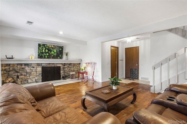 living room with a stone fireplace, light hardwood / wood-style floors, and a textured ceiling