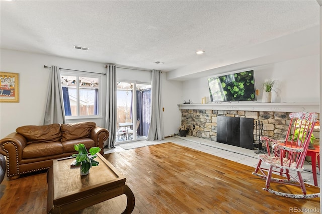 living room featuring a stone fireplace, light hardwood / wood-style flooring, and a textured ceiling