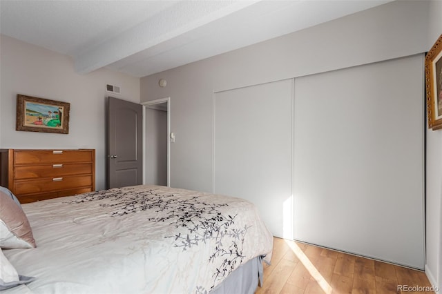 bedroom featuring a closet, hardwood / wood-style floors, and beamed ceiling