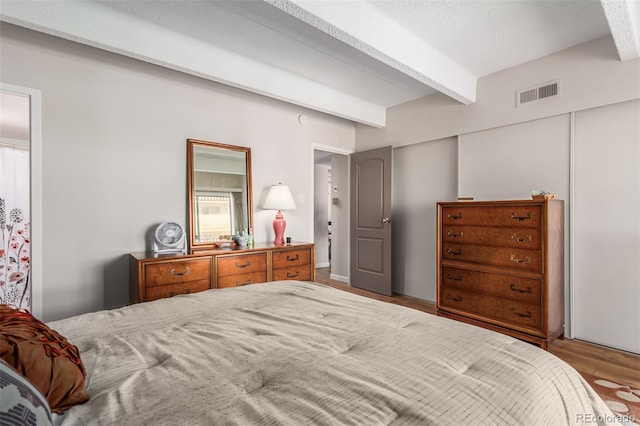 bedroom featuring a textured ceiling, beam ceiling, and light wood-type flooring