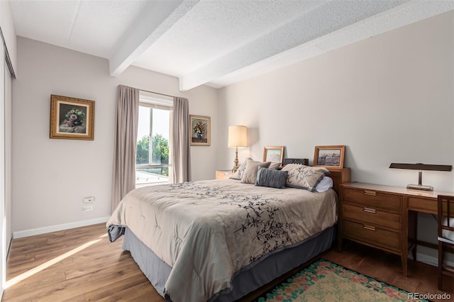 bedroom featuring beam ceiling, a textured ceiling, and light hardwood / wood-style floors