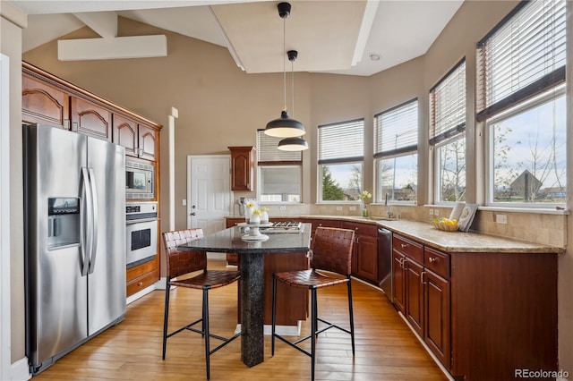 6595 Meade Ct, Arvada, CO 80003 - kitchen featuring stainless steel appliances, light wood finished floors, a kitchen bar, a towering ceiling, and decorative light fixtures