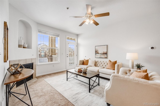 living room with light carpet, ceiling fan, a tiled fireplace, and baseboards