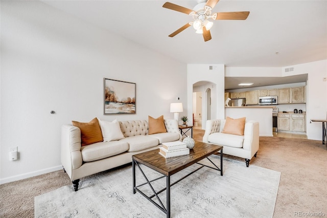 living room with arched walkways, light colored carpet, visible vents, a ceiling fan, and baseboards