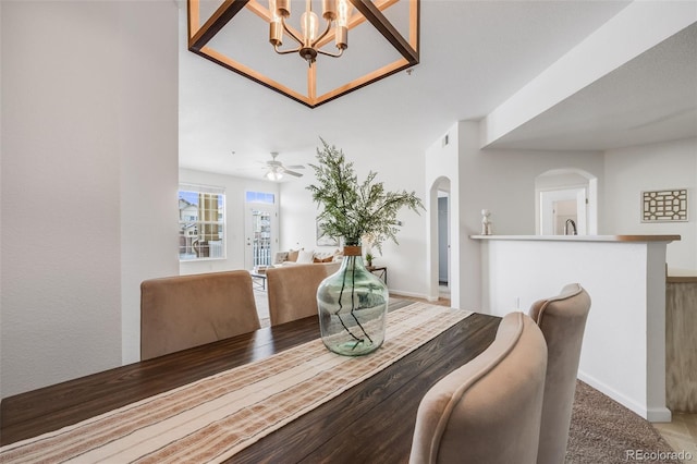 dining space with arched walkways, ceiling fan with notable chandelier, carpet flooring, and baseboards