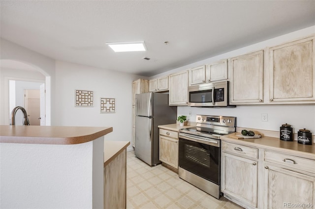 kitchen featuring arched walkways, light brown cabinets, a sink, appliances with stainless steel finishes, and light floors