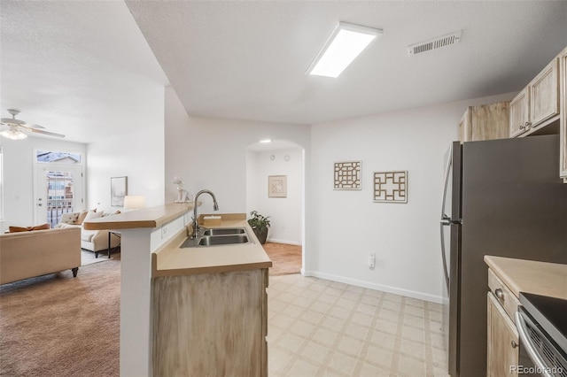 kitchen with visible vents, open floor plan, light floors, light brown cabinets, and a sink