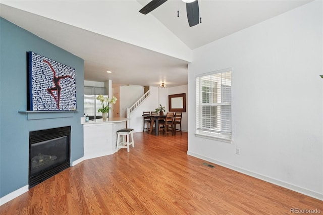 2408 Concord Cir, Lafayette, CO 80026 - living room with stairway, a ceiling fan, light wood-style flooring, a glass covered fireplace, and high vaulted ceiling