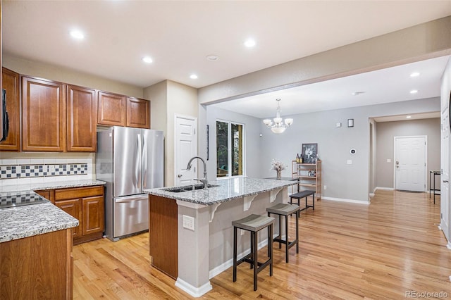 kitchen with stainless steel refrigerator, light stone countertops, hanging light fixtures, an inviting chandelier, and an island with sink