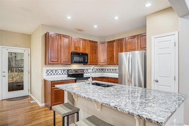 kitchen with light stone countertops, a breakfast bar area, brown cabinetry, stainless steel appliances, and a sink