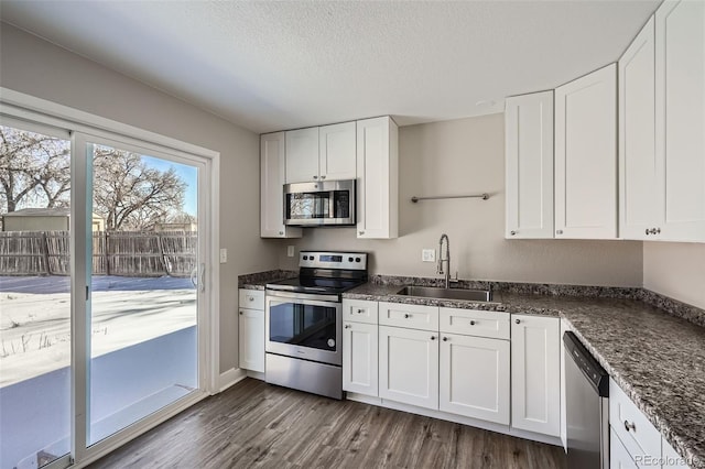 kitchen featuring sink, dark stone countertops, appliances with stainless steel finishes, dark hardwood / wood-style flooring, and white cabinets