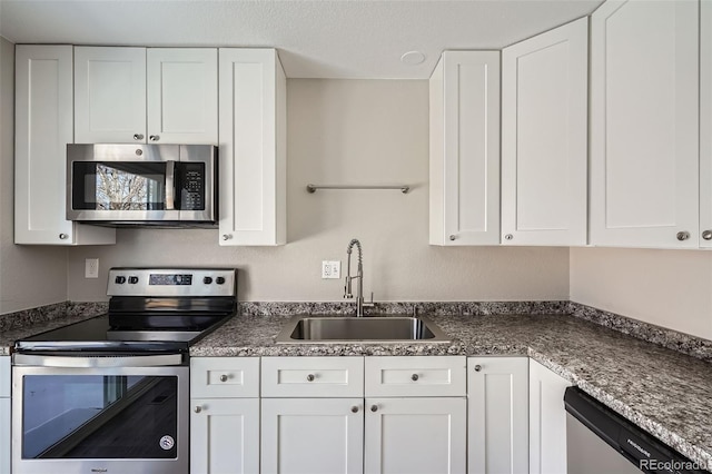 kitchen featuring appliances with stainless steel finishes, sink, white cabinets, and dark stone counters