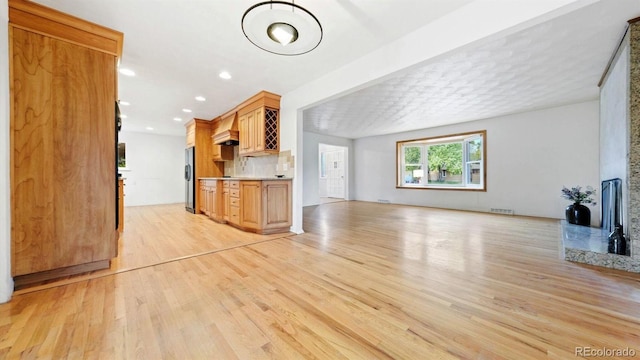 kitchen featuring tasteful backsplash, light hardwood / wood-style flooring, premium range hood, and stainless steel refrigerator with ice dispenser