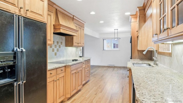 kitchen featuring black appliances, sink, hanging light fixtures, light hardwood / wood-style flooring, and premium range hood