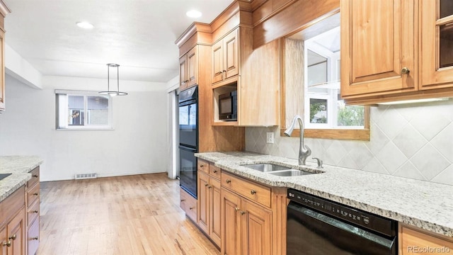 kitchen featuring hanging light fixtures, light stone counters, light hardwood / wood-style flooring, black appliances, and sink