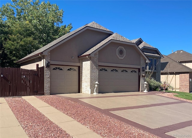 view of front facade featuring an attached garage, brick siding, fence, concrete driveway, and stucco siding